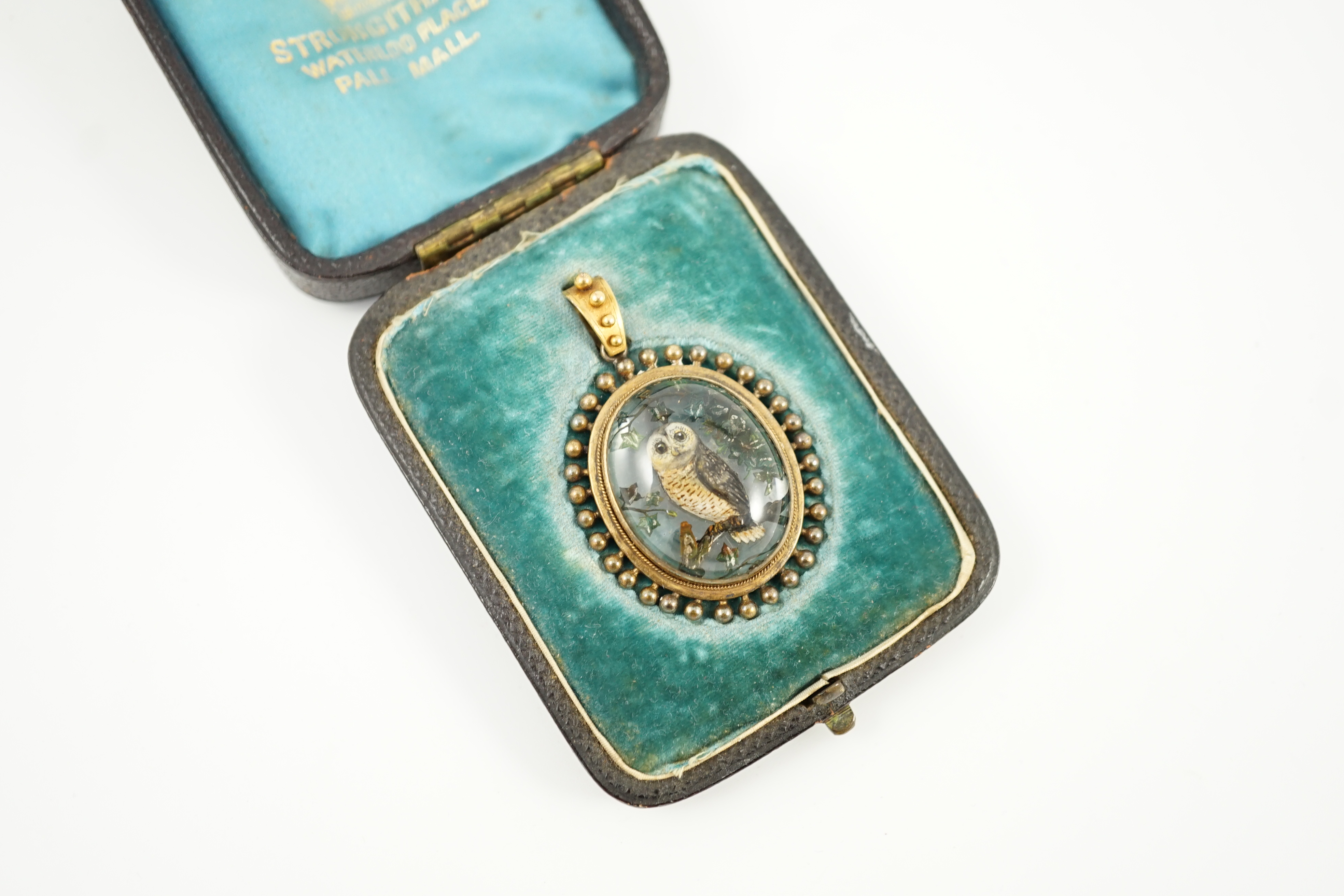 A Victorian yellow metal mounted Essex crystal oval pendant, depicting an owl upon a branch, amid foliage